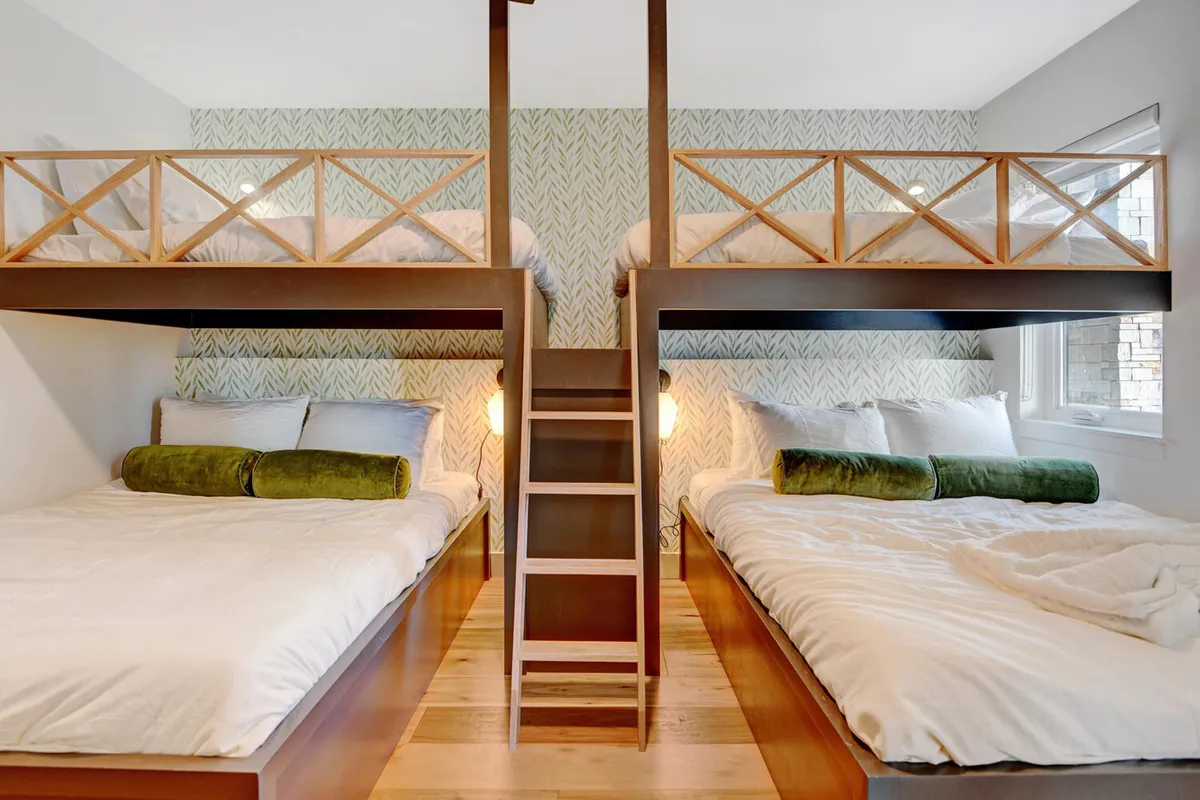 A playful custom bunk room with sturdy wooden bunk beds, green accent pillows, and a wooden ladder. The room is styled to be cozy and inviting, perfect for children or groups wanting to relax together, and includes thoughtful touches for comfort and fun.