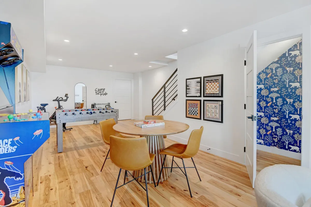 A vibrant interior space designed for entertainment, showing an arcade game, foosball table, dining table, and creative wall art. The layout invites group activities, laughter, and game nights, with ample space for children and adults to interact.