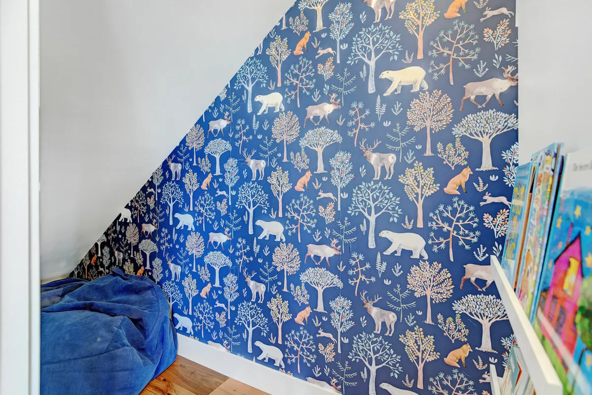 A whimsically decorated nook with animal-patterned wallpaper, a blue bean bag, and a colorful bookshelf. The small scale and playful design signal a space designed just for young children, ideal for reading, imaginative play, and quiet moments.
