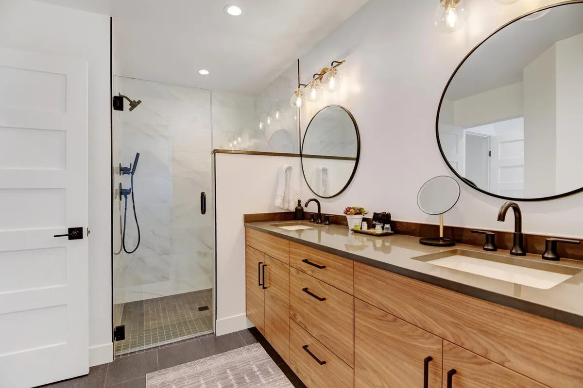 A modern, spa-inspired bathroom with a double vanity, expansive mirrors, and a glass-enclosed shower. The space is bright and inviting, perfect for morning routines or evening relaxation, and exudes a sense of luxury and thoughtful design.