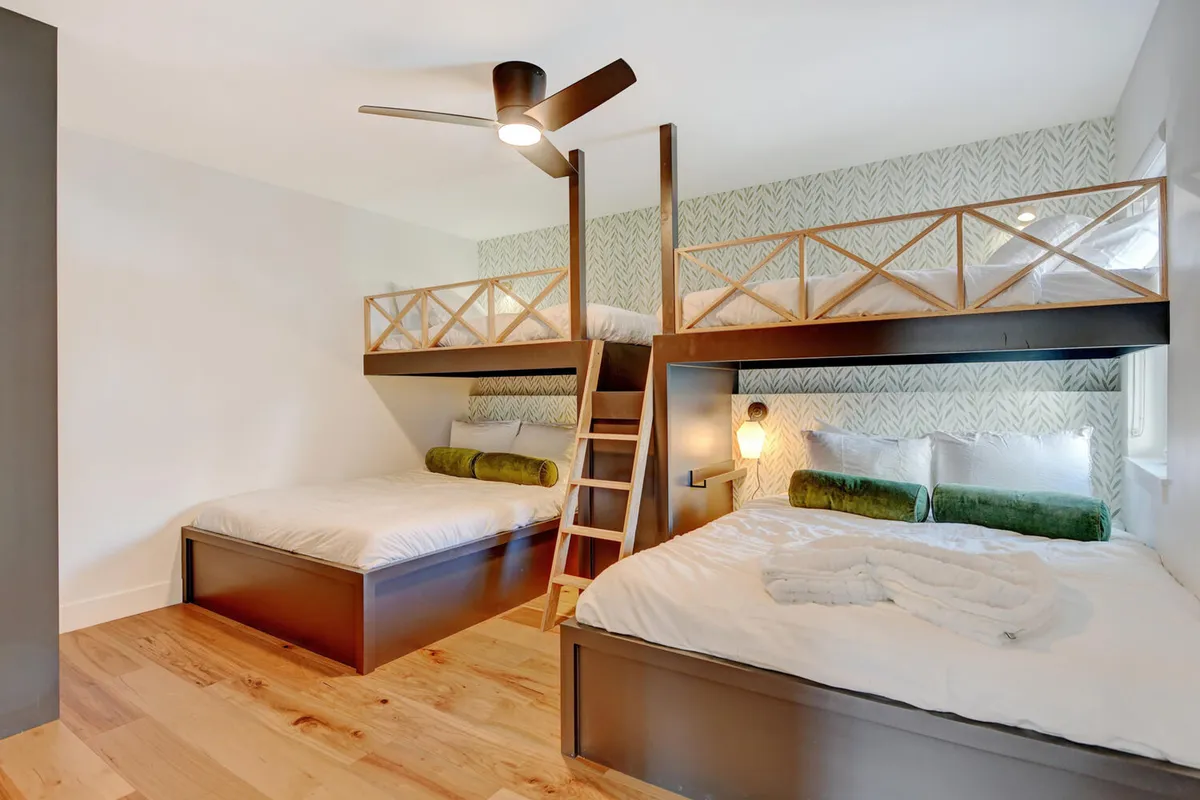 A cozy, playful bunk room featuring bunk beds with a wooden ladder, green accents, and a whimsical light fixture. The space is designed for kids to enjoy bedtime stories, games, and socializing in a relaxed environment.